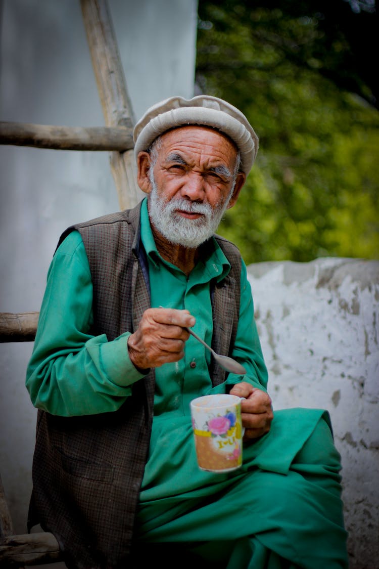 Elderly Man Holding A Mug And A Spoon