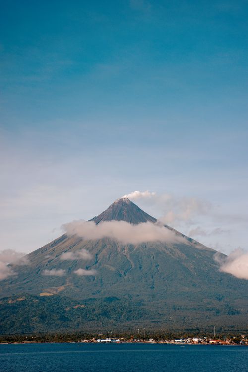 Free Picturesque view of a volcano with a clear sky, surrounded by lush greenery and calm sea. Stock Photo