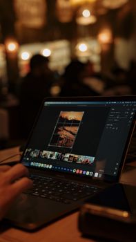 Person editing photos on a laptop in a dimly lit cafe, creating a cozy ambiance.