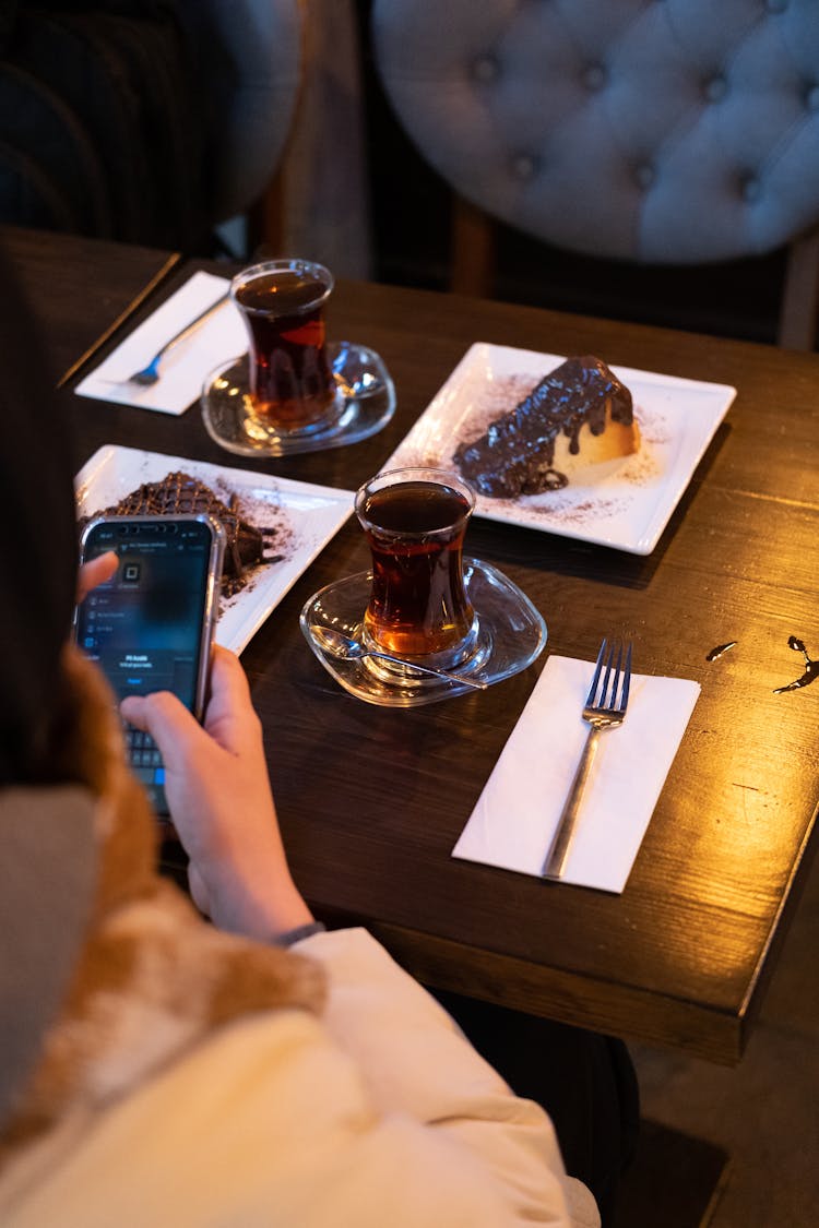 Woman Using A Phone Over A Table With Plates Of Food