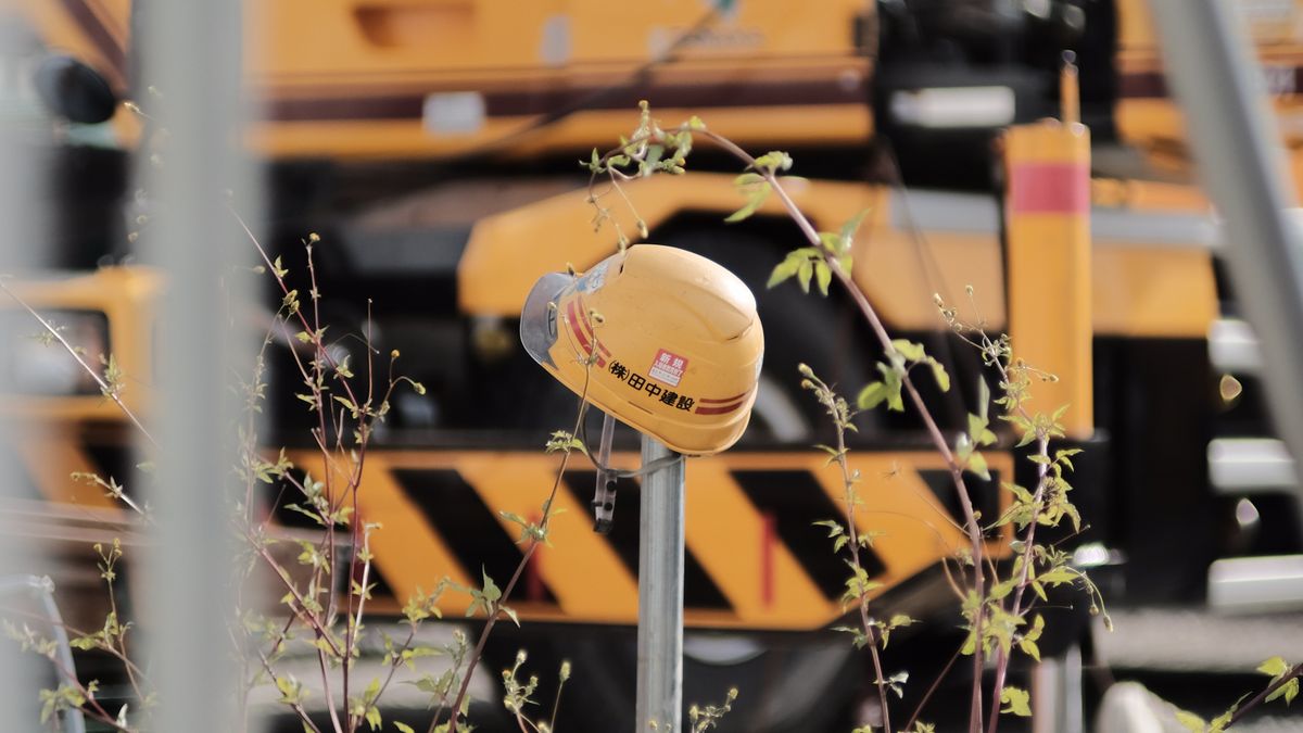 A yellow safety helmet hung on a post at a construction site with a mobile crane behind