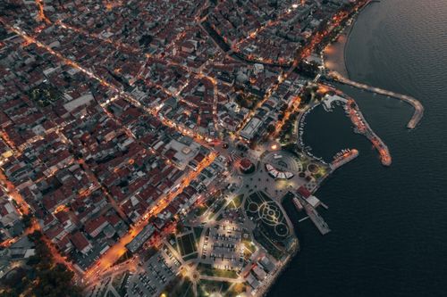 Free Stunning aerial view of a vibrant coastal city illuminated at dusk, showcasing bustling streets and waterfront. Stock Photo