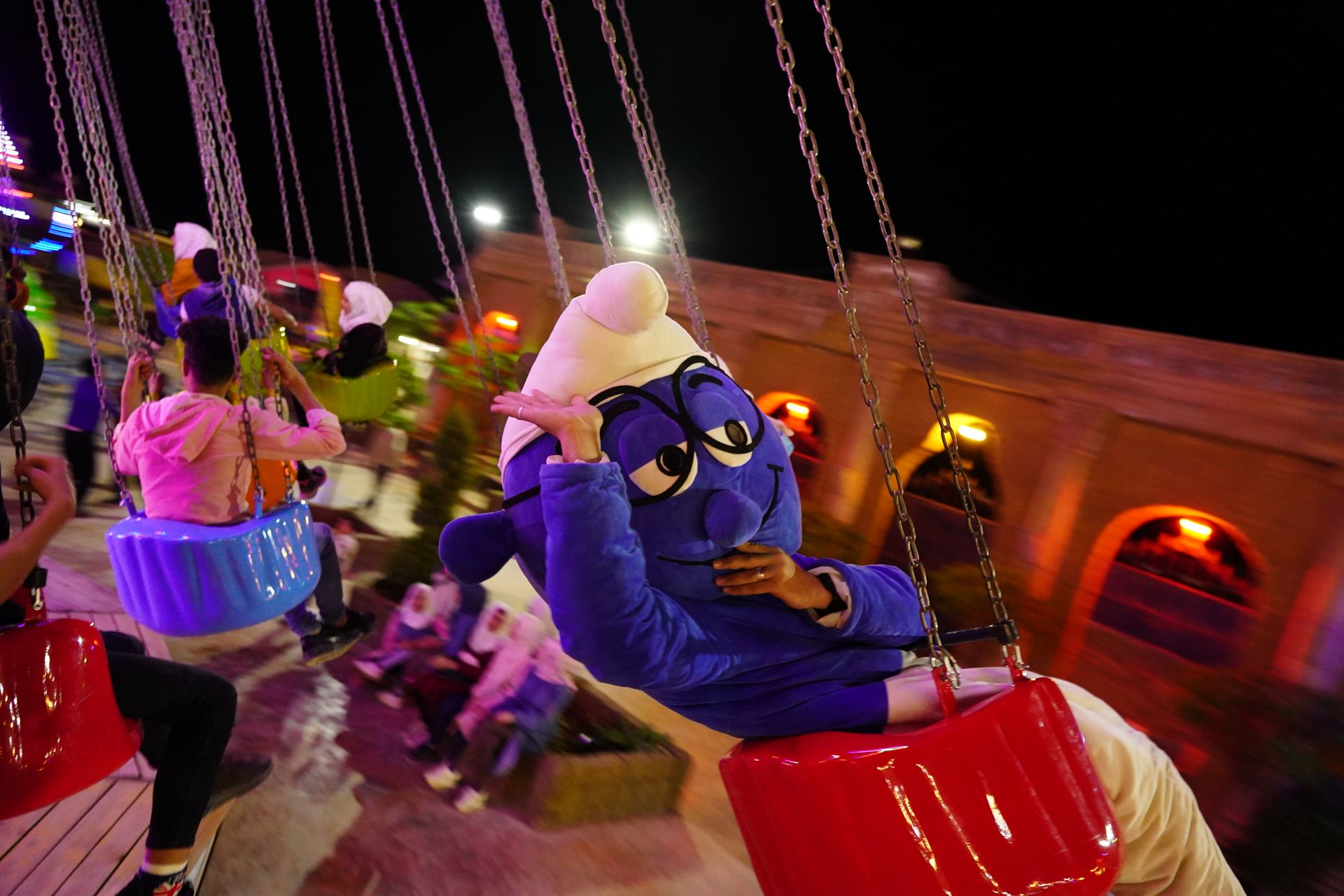 A fun night at an amusement park featuring a costumed mascot enjoying a thrilling swing ride.