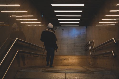 Free A woman walks down a dimly lit staircase in an underground subway station, wearing a scarf and hat. Stock Photo