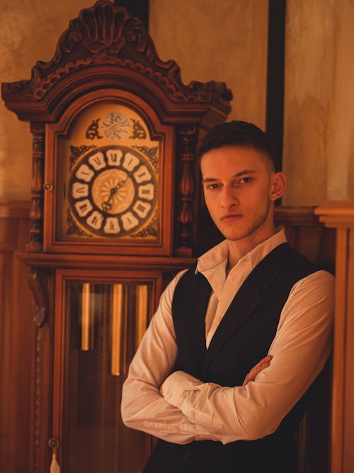 Free A Man in White Long Sleeves and Black Vest Near a Wooden Clock Stock Photo