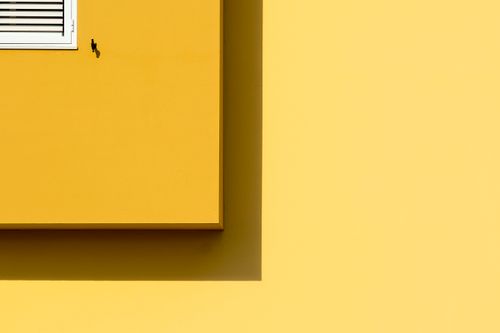 Free A minimalist yellow wall featuring a sunlit window with sharp shadows. Stock Photo