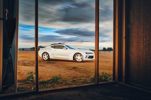 日落时分，从质朴的窗框望去，一辆白色科迈罗停在开阔的田野上