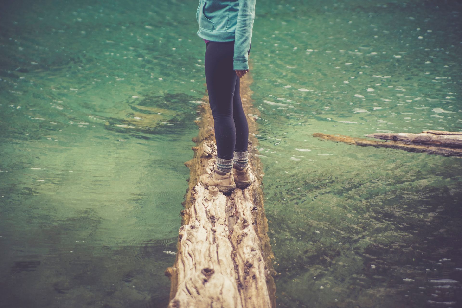 Person Standing on a Brown Wood Log Floating on a Body of Water