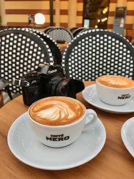 Two lattes with beautiful foam art placed on a cafe table alongside a camera, creating a warm and inviting scene.