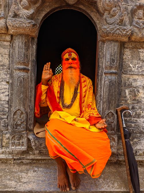 Free A holy man in vibrant attire sits in a stone temple window in Kathmandu, Nepal. Stock Photo