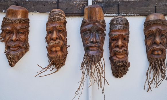 A set of handmade carved wooden tribal masks hanging on a wall.