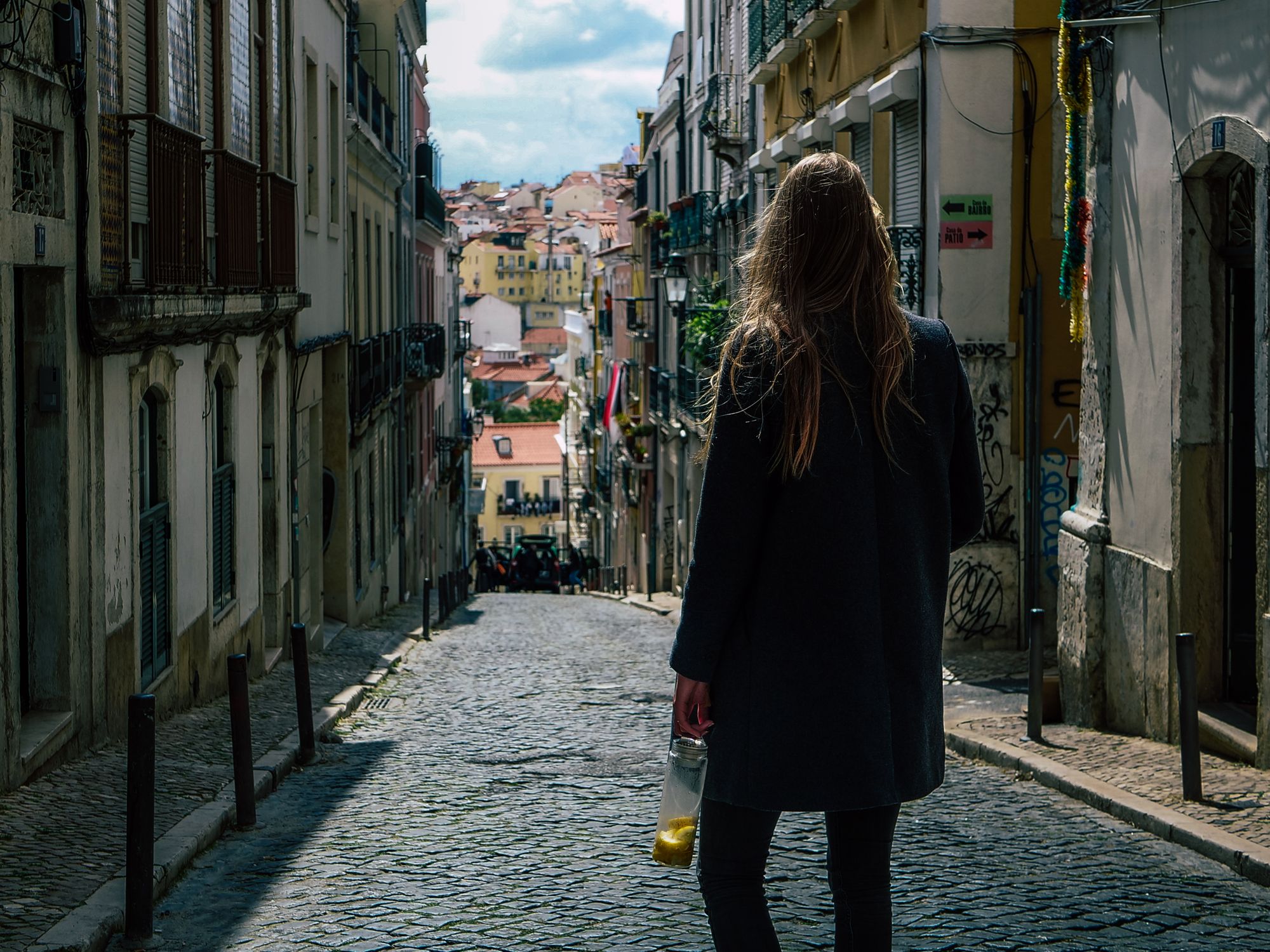 A woman with a jar of lemons walks down a cobblestone street in Lisbon, capturing the urban charm.