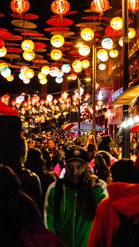 Colorful street festival at night with bright lanterns and a busy crowd celebrating outdoors.