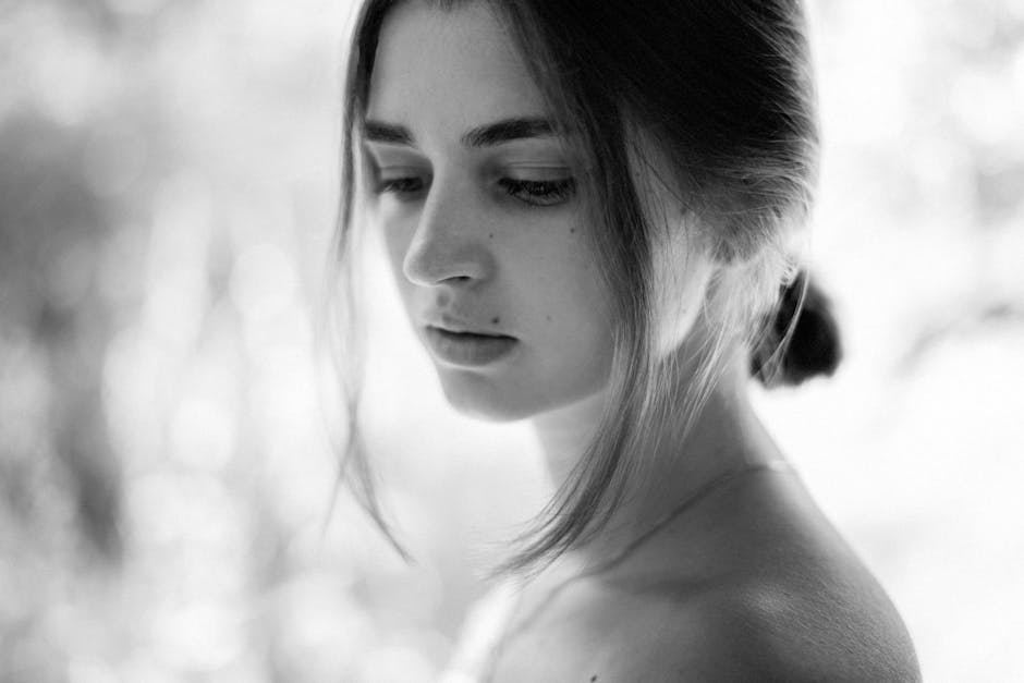 A contemplative black and white portrait of a woman with soft lighting and a blurred background.