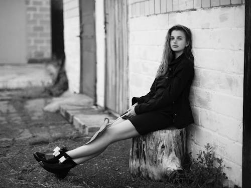 Free Woman in Black Long Sleeve Dress Sitting on Concrete Wall Stock Photo