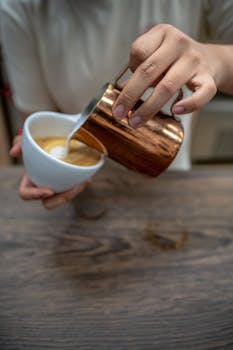 Close-up of a barista creating latte art in a coffee cup indoors.