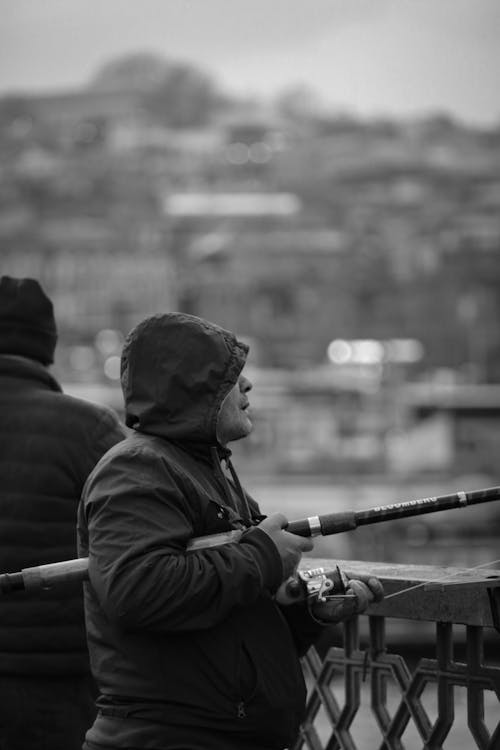 Grayscale Photo of Man in Hoodie holding a Fishing Rod 