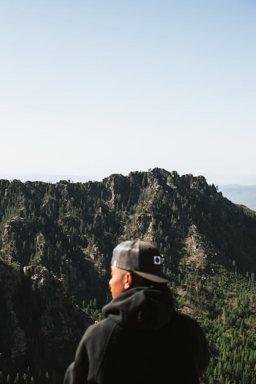 A Man Wearing a Hoodie and a Cap Looking at a Beautiful View of Mountains