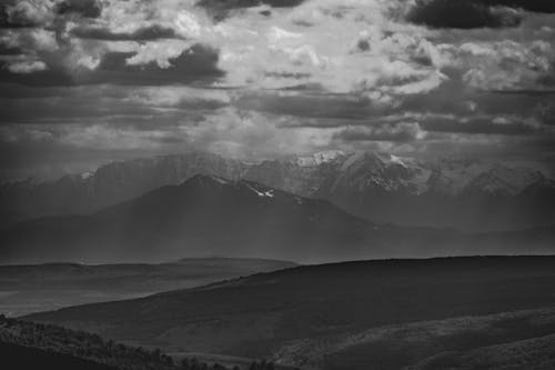 Grayscale Photo of Mountain Ranges Under Cloudy Sky