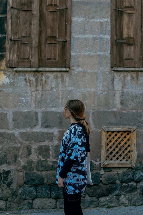 Woman in Printed Shirt Standing Beside a Stone House
