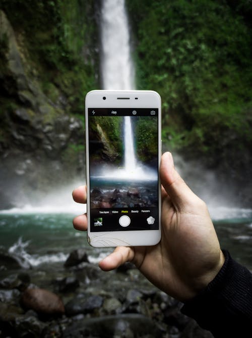 Free A Person Taking a Picture of a Waterfall with a Smartphone Stock Photo