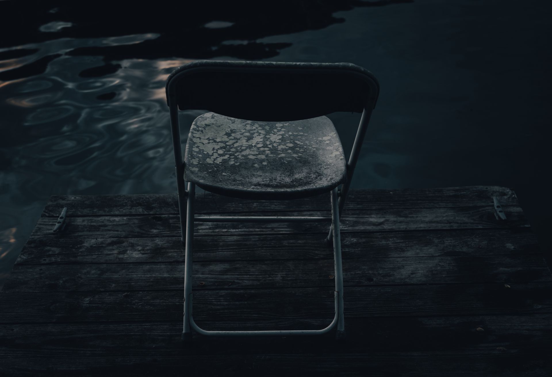 Black and Gray Folding Chair on a Wooden Deck Near a Body of Water