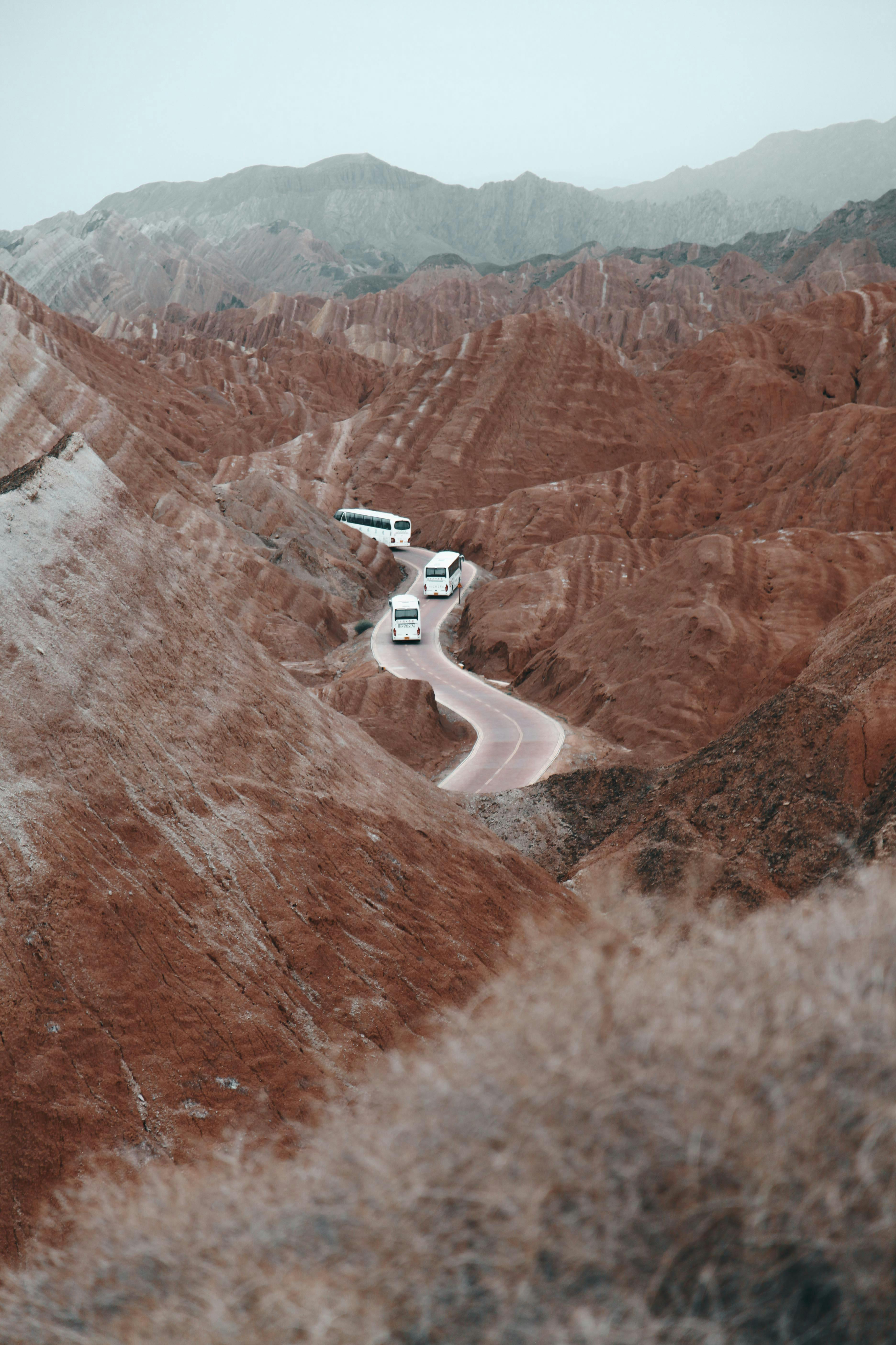 Spectacular view of buses navigating a winding road through the red sandstone mountains of Zhangye Danxia, China.