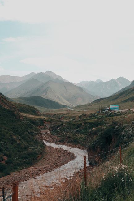 Picturesque mountain stream flowing through green valleys in Qinghai, China under a cloudy sky.