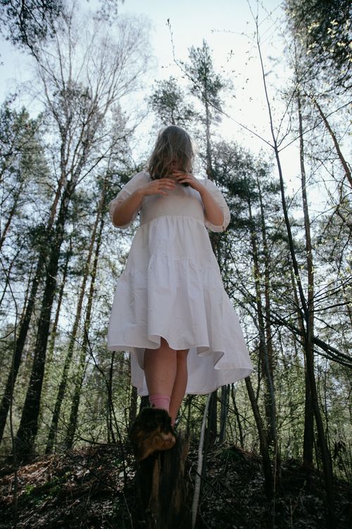 Free Low angle shot of a woman in a white dress standing in a forest, surrounded by tall trees. Stock Photo