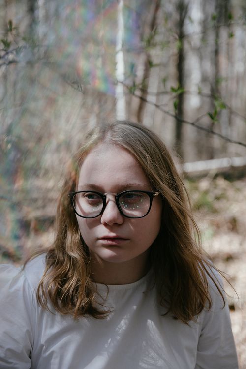 Free A reflective portrait of a woman in glasses set against a serene wooded backdrop. Stock Photo