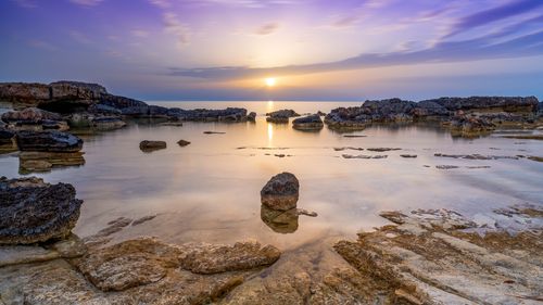 Free Peaceful sunset over a rocky tide pool with calm ocean and vibrant sky. Stock Photo