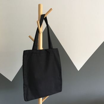 A black canvas tote bag hanging from a wooden peg rack, photo by Stephanie Ho on Pexels