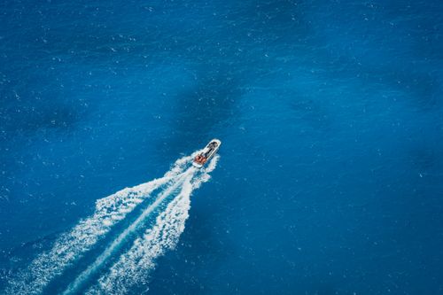 Free A speed boat cuts through the deep blue ocean in an aerial shot, creating a dynamic wake. Stock Photo