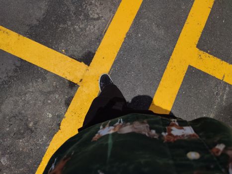Person standing on marked asphalt with visible yellow lines. High angle photo.