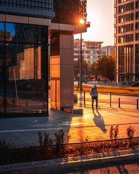A person walks through modern architecture in Warsaw during a warm sunset.