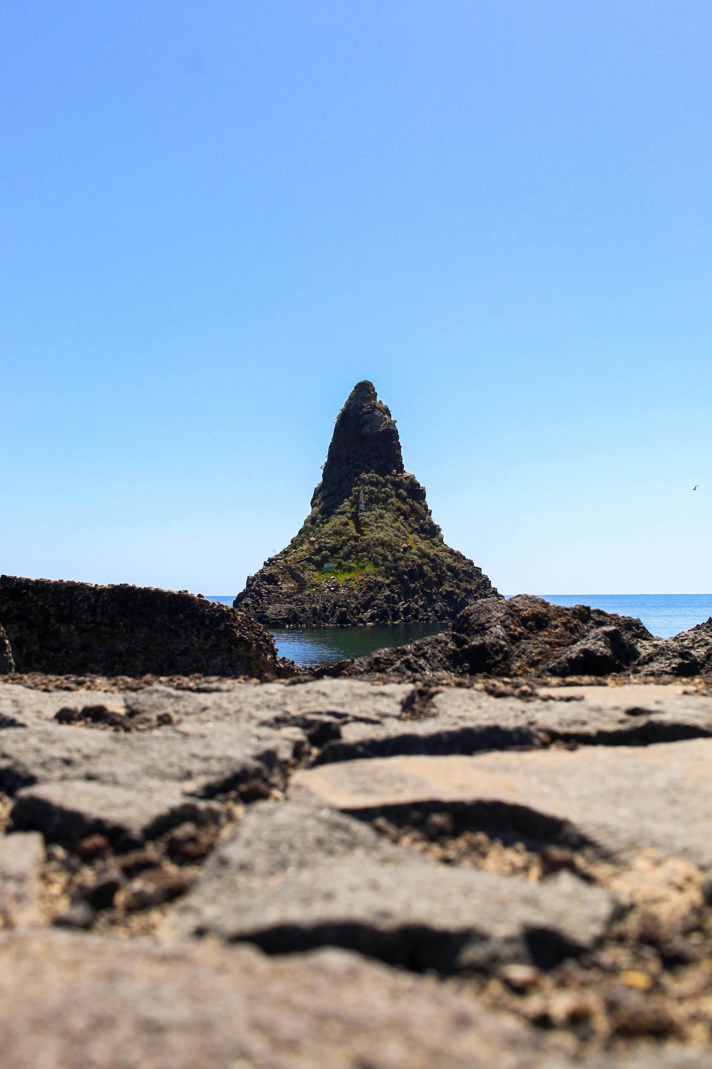 A striking geological sea stack rises from the ocean under a clear blue sky.