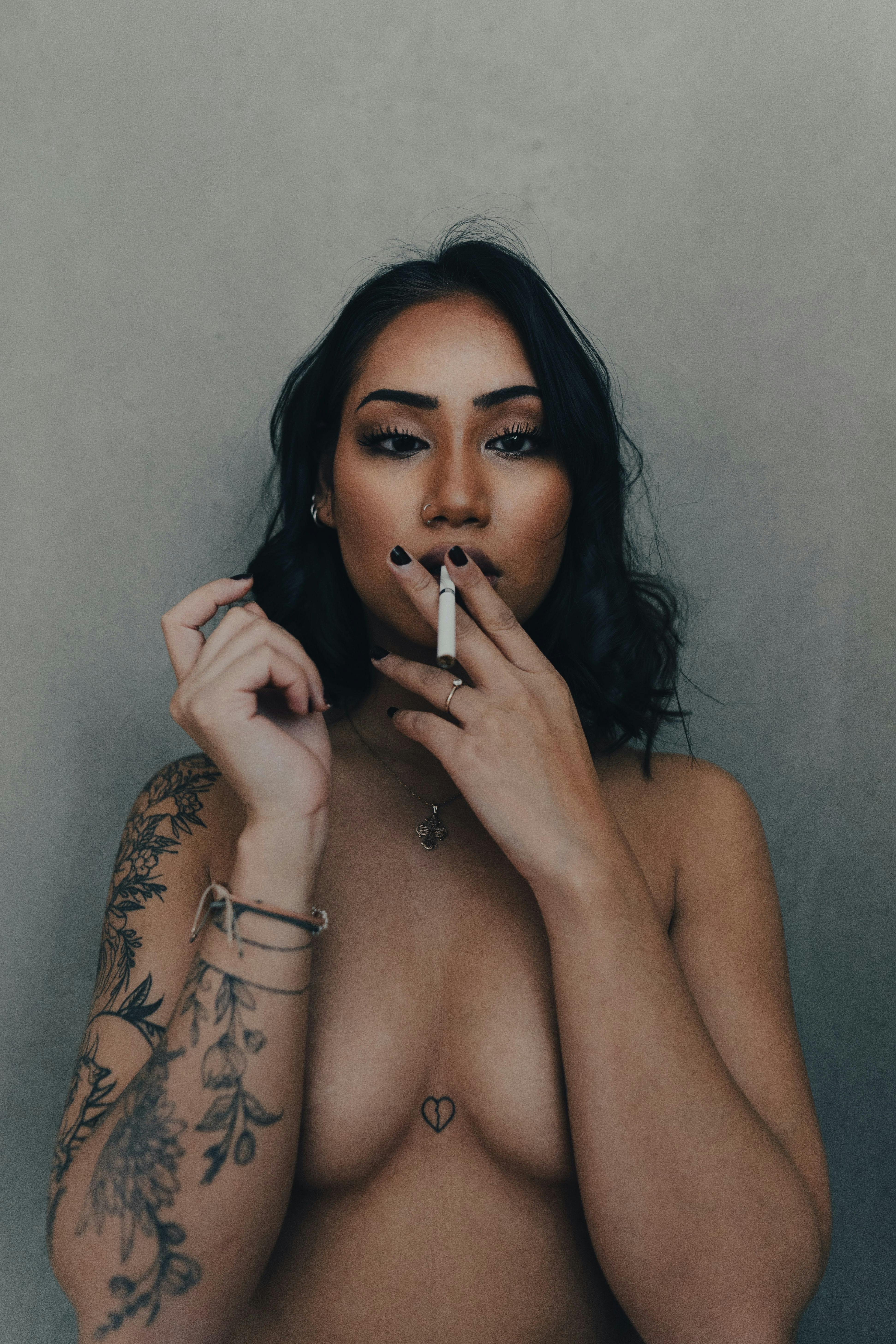 nude tattooed brunette woman smoking cigarette