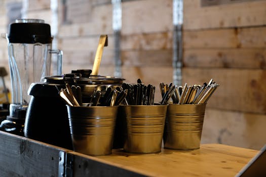 Close-up of stainless steel cutlery in metal buckets on a rustic kitchen table.