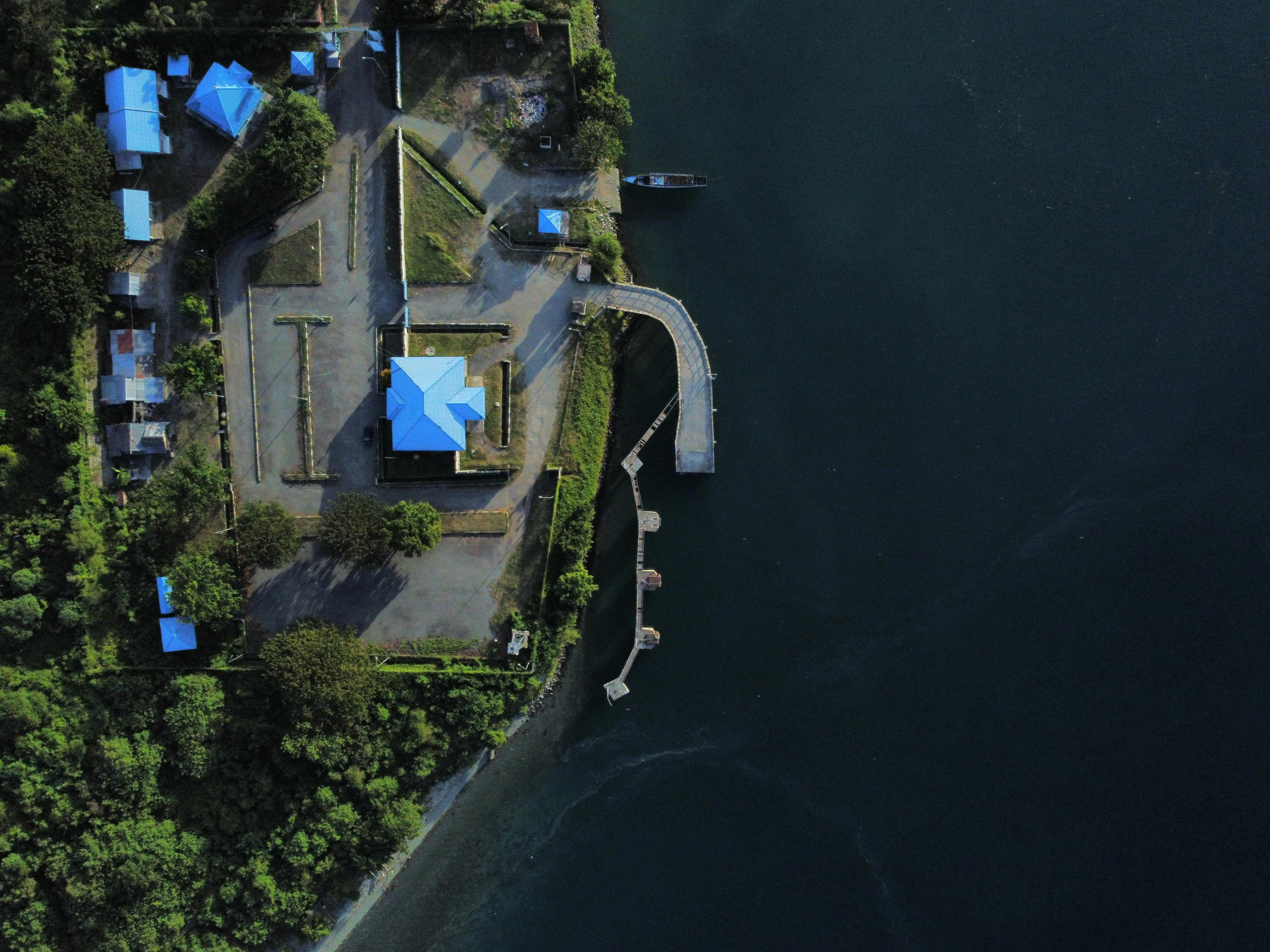 Drone capture of a lakeside property with blue-roofed buildings and a dock in a scenic landscape.