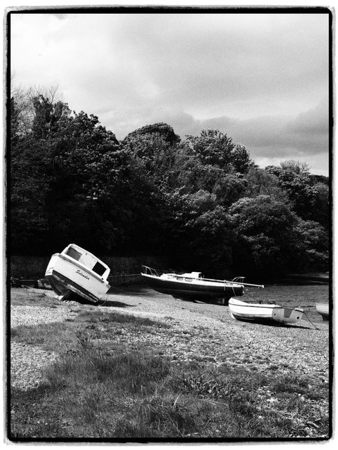 Black and white image of boats on a deserted shore with lush forest backdrop.