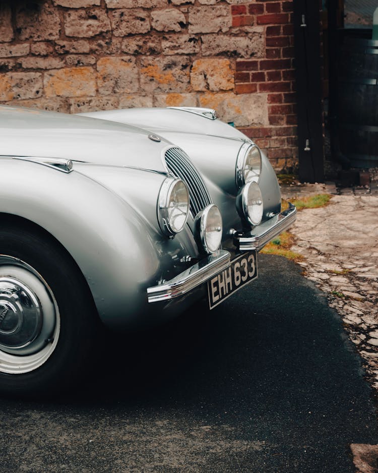 Silver Classic Car Parked Beside A Stone Wall