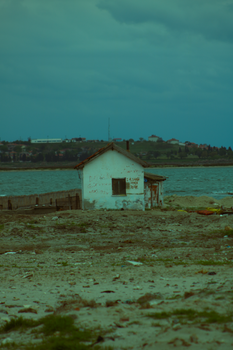 A lonely, abandoned hut stands by the beach on a cloudy, stormy day.