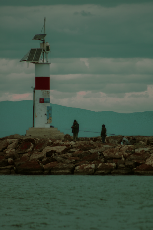Free Fishermen near a solar-powered lighthouse on a rocky breakwater by the sea. Stock Photo