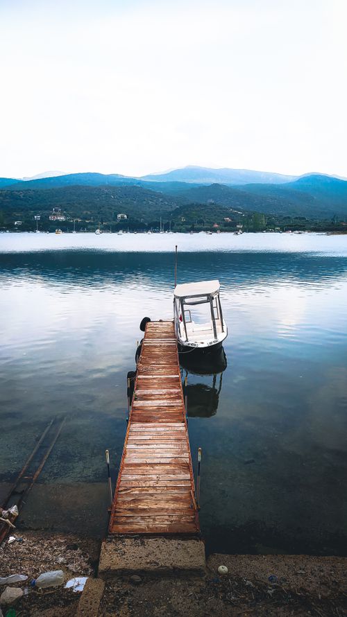 Free A peaceful wooden dock extending into a serene Turkish lake with a small boat. Perfect for travel and nature themes. Stock Photo
