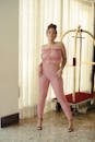 Woman in Pink Spaghetti Strap Top and Pink Pants Standing Beside White Window Curtain