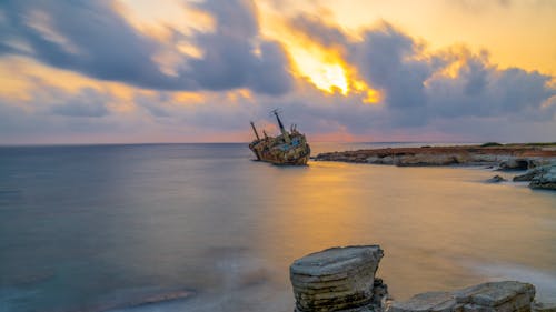 Free Brown Ship on Sea Under Cloudy Sky during Sunset Stock Photo