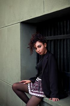 Woman in fashionable attire sitting against a building in Tehran, showcasing street style.