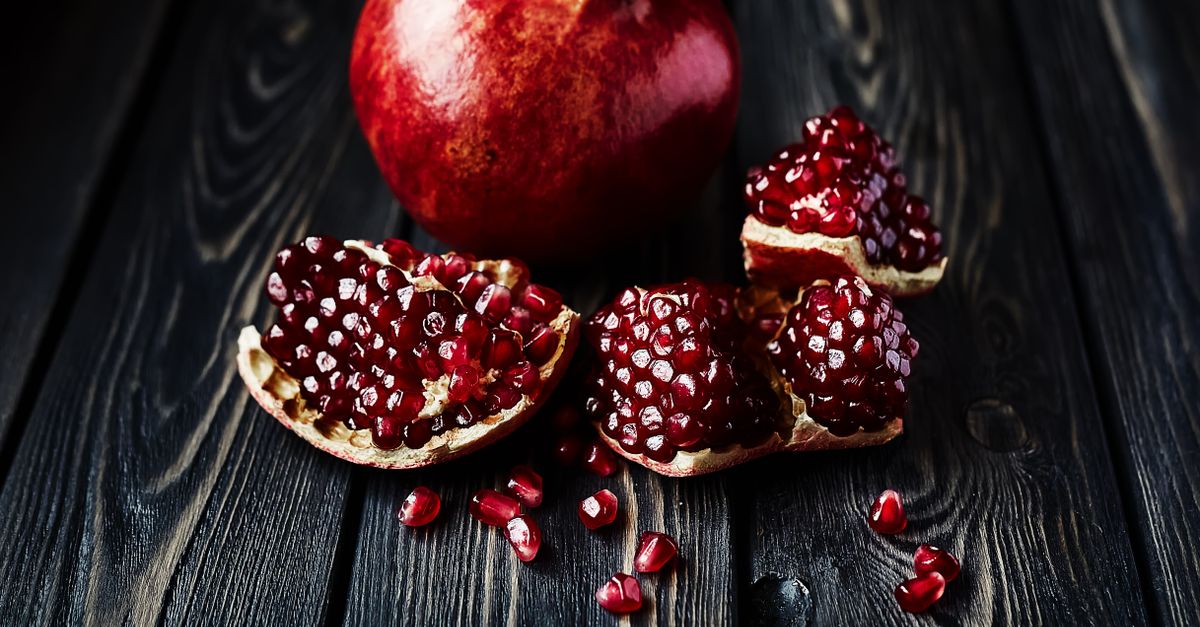 Vivid close-up of fresh organic pomegranate on a rustic wooden surface with scattered seeds. - Evidence evidence guide for pomegranate exercise recovery randomized trial
