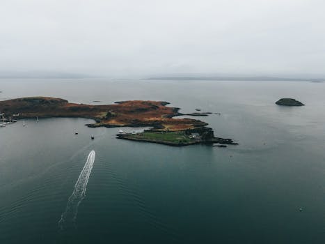 Drone shot capturing a tranquil island surrounded by a vast ocean with a boat trail.