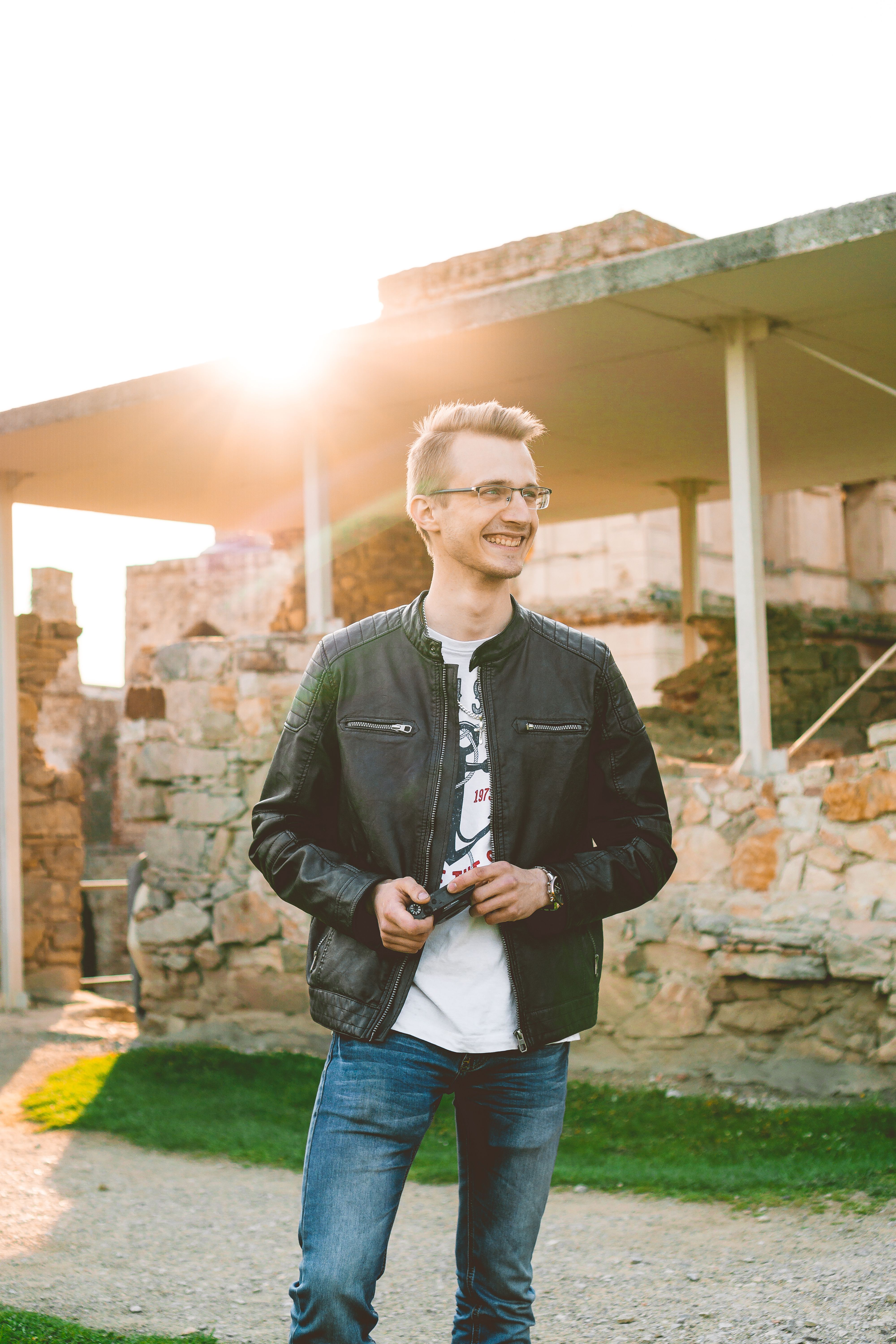 Smiling man in a black leather jacket outdoors with sunset lighting.